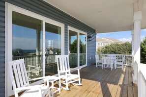Settle into your rocking chair on this peaceful covered deck, where you can watch the day unfold while enjoying glimpses of the ocean through the neighborhood greenery. - Second Row Ocean View Retreat w/ Pool and Elevator (Emerald Isle)