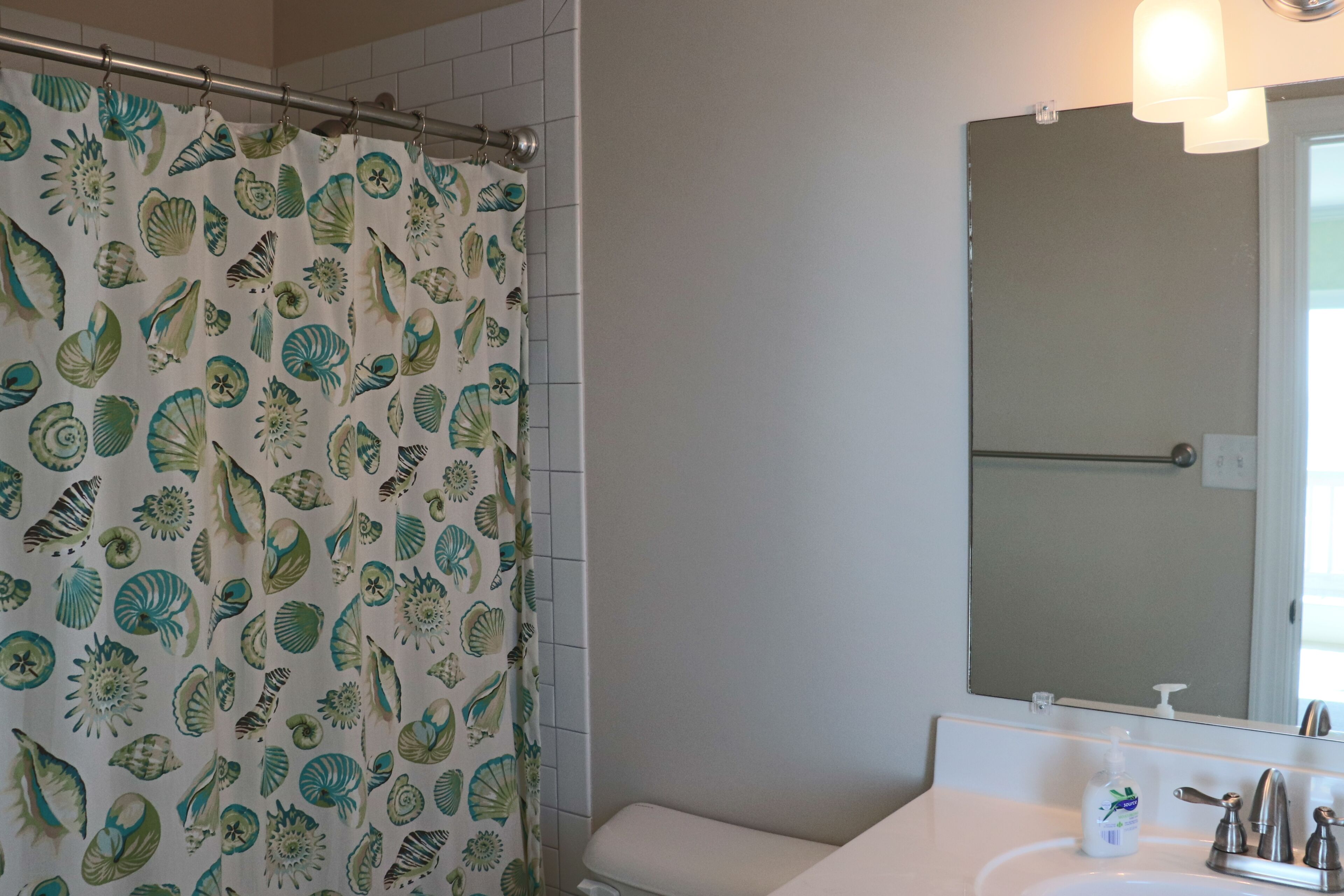 Un bagno con tenda da doccia a motivo di conchiglie, un lavandino bianco con dispenser di sapone e uno specchio sopra il lavandino.