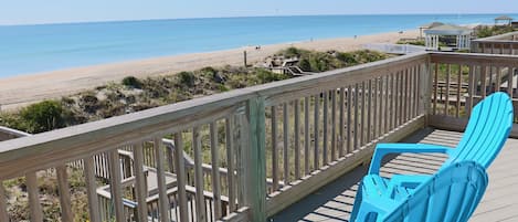 Une terrasse en bois avec une rambarde, deux chaises Adirondack bleues et une vue sur la plage.