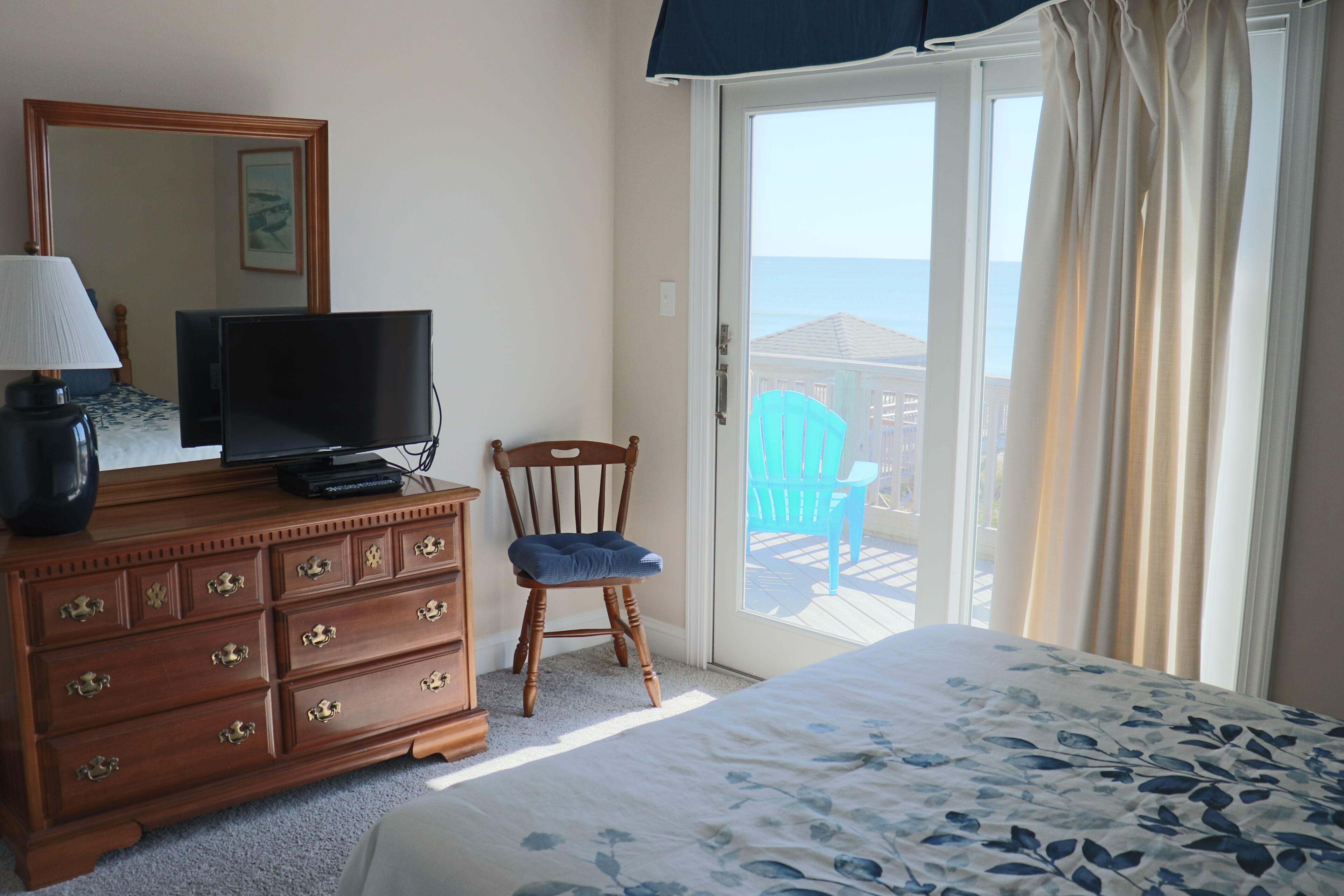 Une chambre à coucher comprenant un lit, une commode avec des tiroirs, un téléviseur, une chaise et un balcon avec vue.