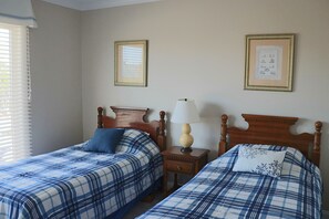 Ein Schlafzimmer mit zwei Betten, einem Nachttisch, einer Lampe und zwei gerahmten Bildern an der Wand.