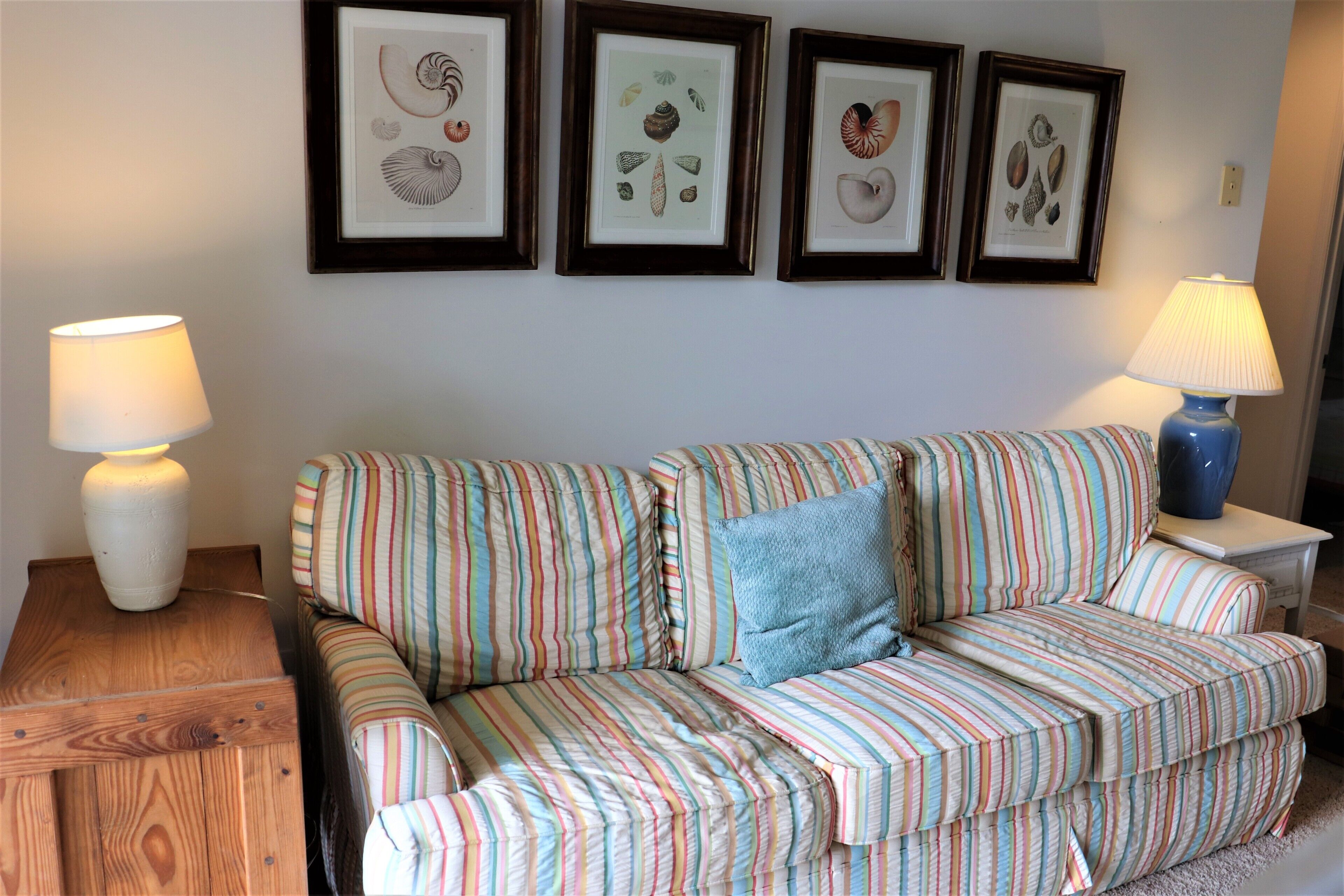 A striped sofa with a blue pillow, two side tables with lamps, and framed botanical prints on the wall.