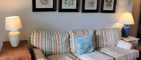 A striped sofa with a blue pillow, two side tables with lamps, and framed botanical prints on the wall.