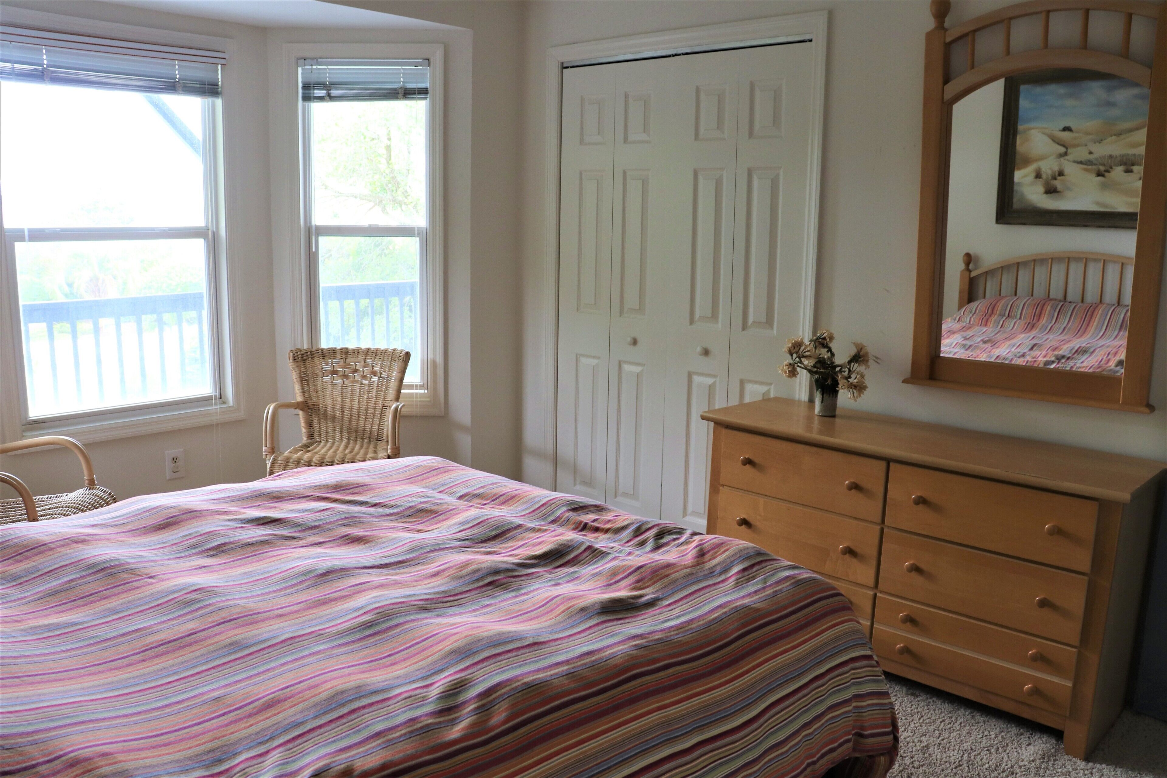 Un dormitorio con cama, cómoda, silla y una puerta con espejo e imagen.