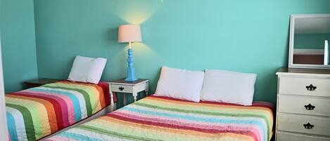 A room with two beds, a nightstand with a lamp, a dresser with drawers, and a mirror.