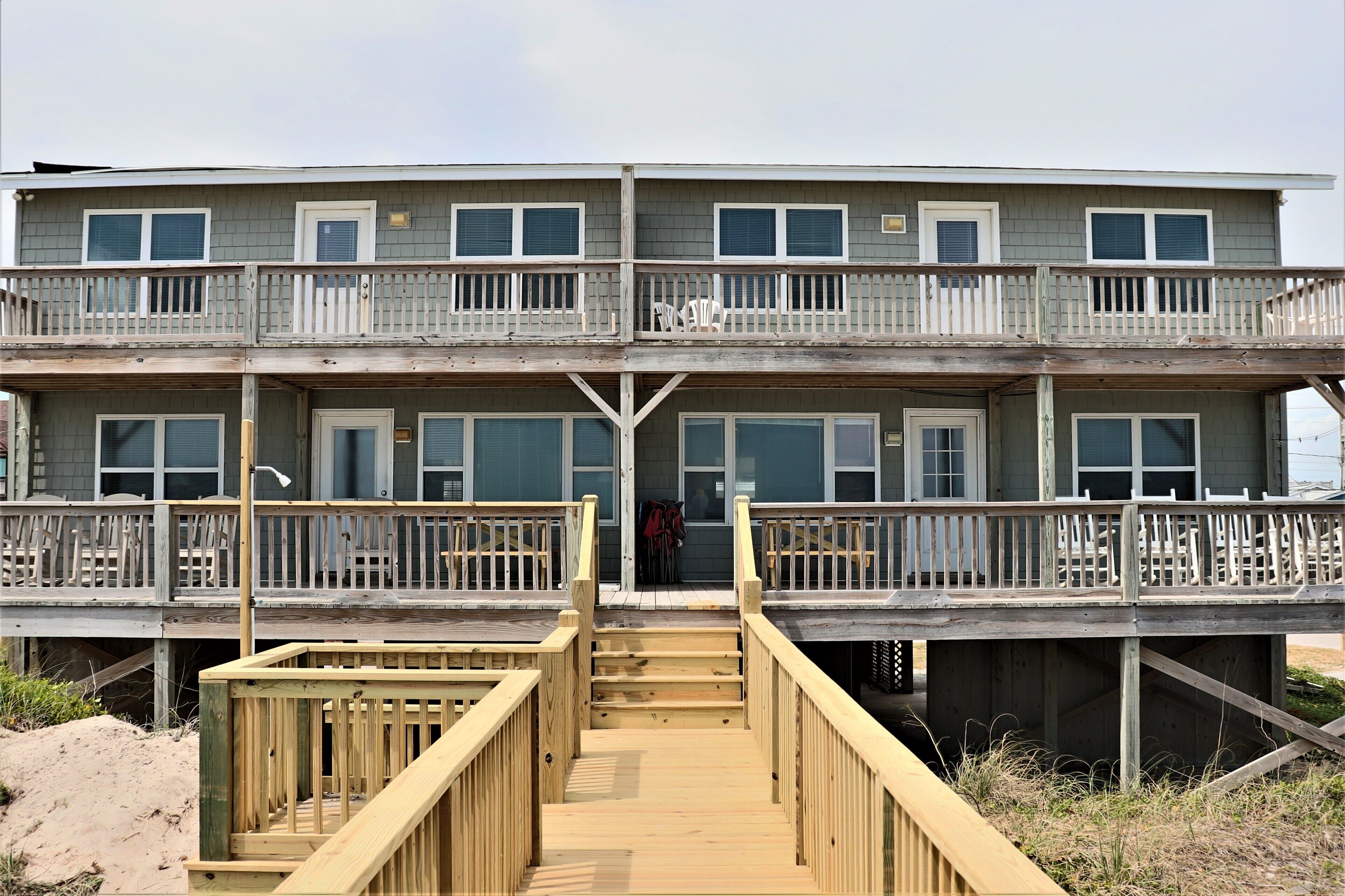 A multi-story building with balconies, a wooden deck, and a staircase leading to the entrance.