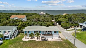 Une maison située sur la côte, dotée d’un balcon, entourée d’une végétation luxuriante et offrant une vue sur la mer.