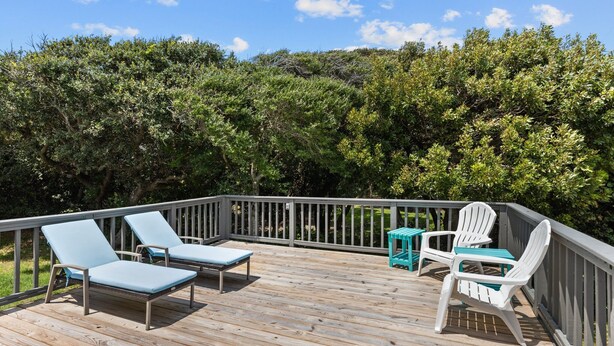 Une terrasse en bois, agrémentée de chaises longues et d’une table, entourée d’une végétation luxuriante.
