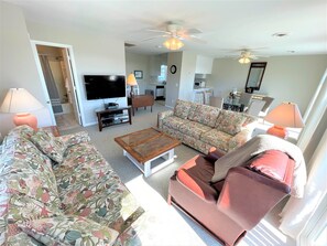 Ein Wohnzimmer mit zwei Sofas, einem Couchtisch, einem Fernseher und Deckenventilatoren.