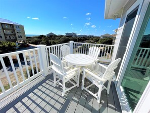 Ein Balkon mit weißem Tisch und Stühlen, einem weißen Geländer und Blick auf das Meer und weitere Gebäude.