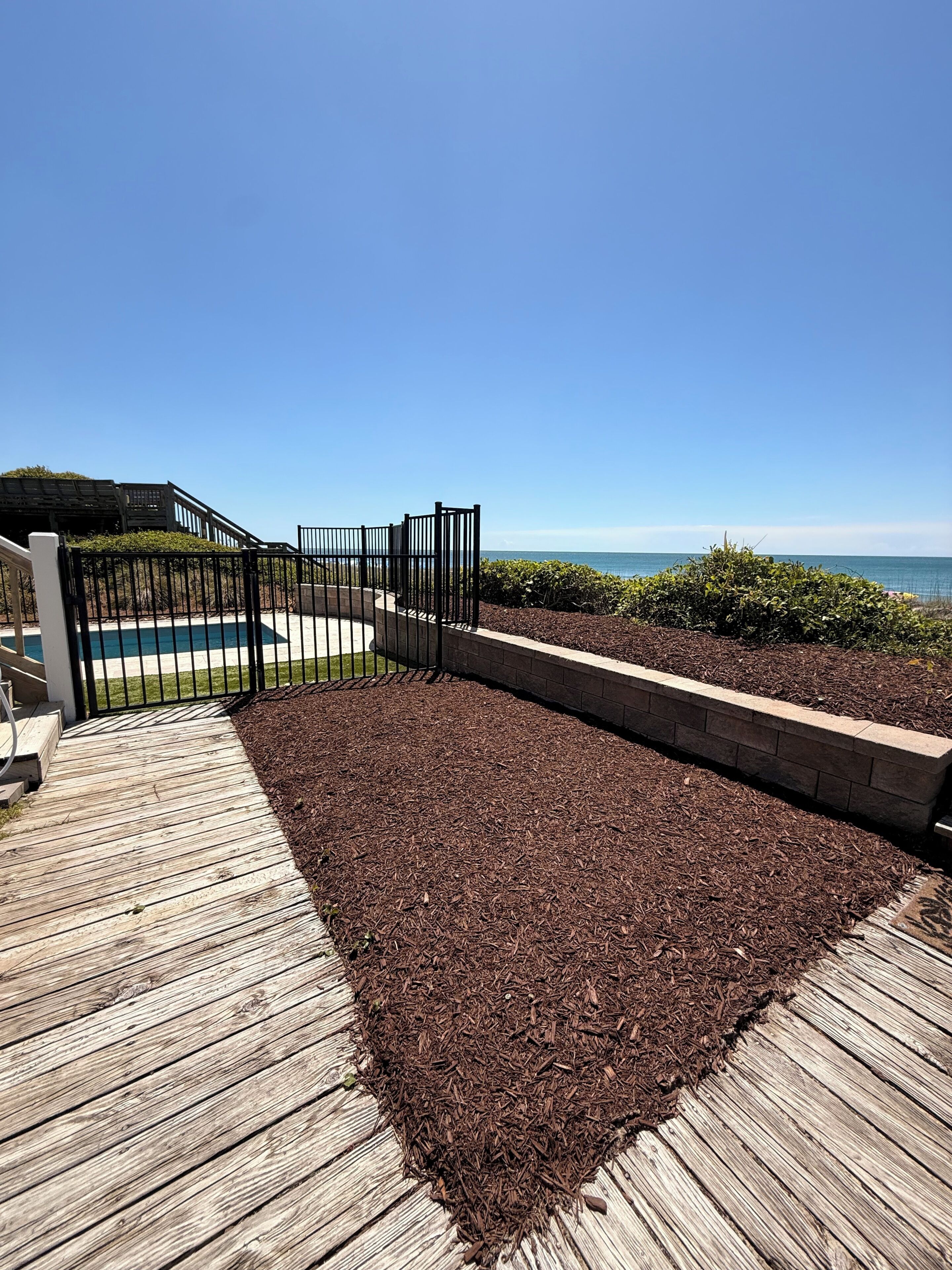 A wooden deck leading to a pool area with a view of the ocean.
