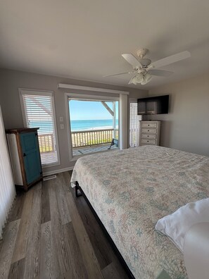 Una camera da letto con un letto, un ventilatore a soffitto, una televisione e vista sulla spiaggia.