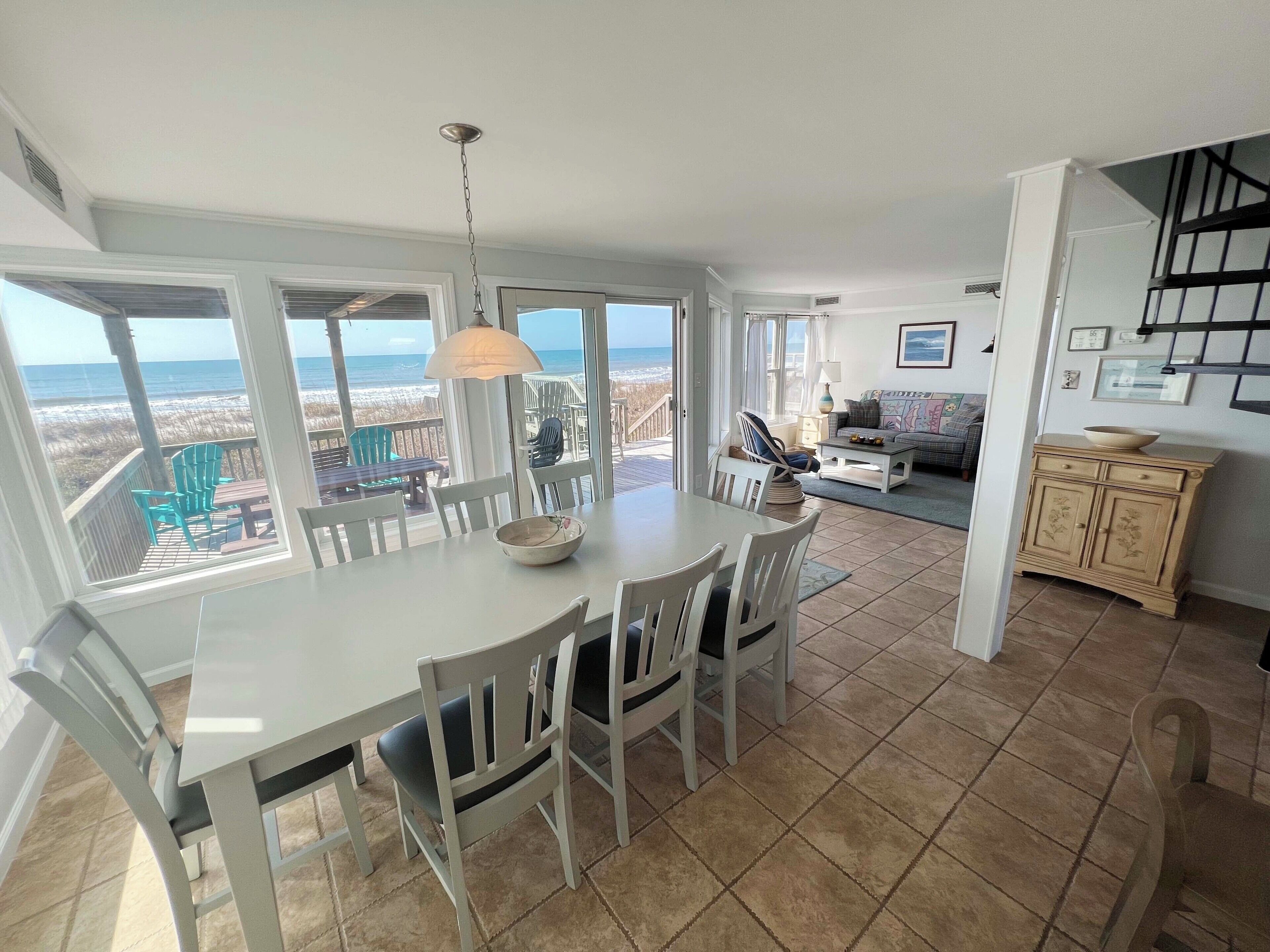 A spacious living area with a dining table, chairs, a sofa, and a view of the beach.