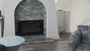 Una sala de estar con chimenea, un televisor montado encima y un sillón estampado.