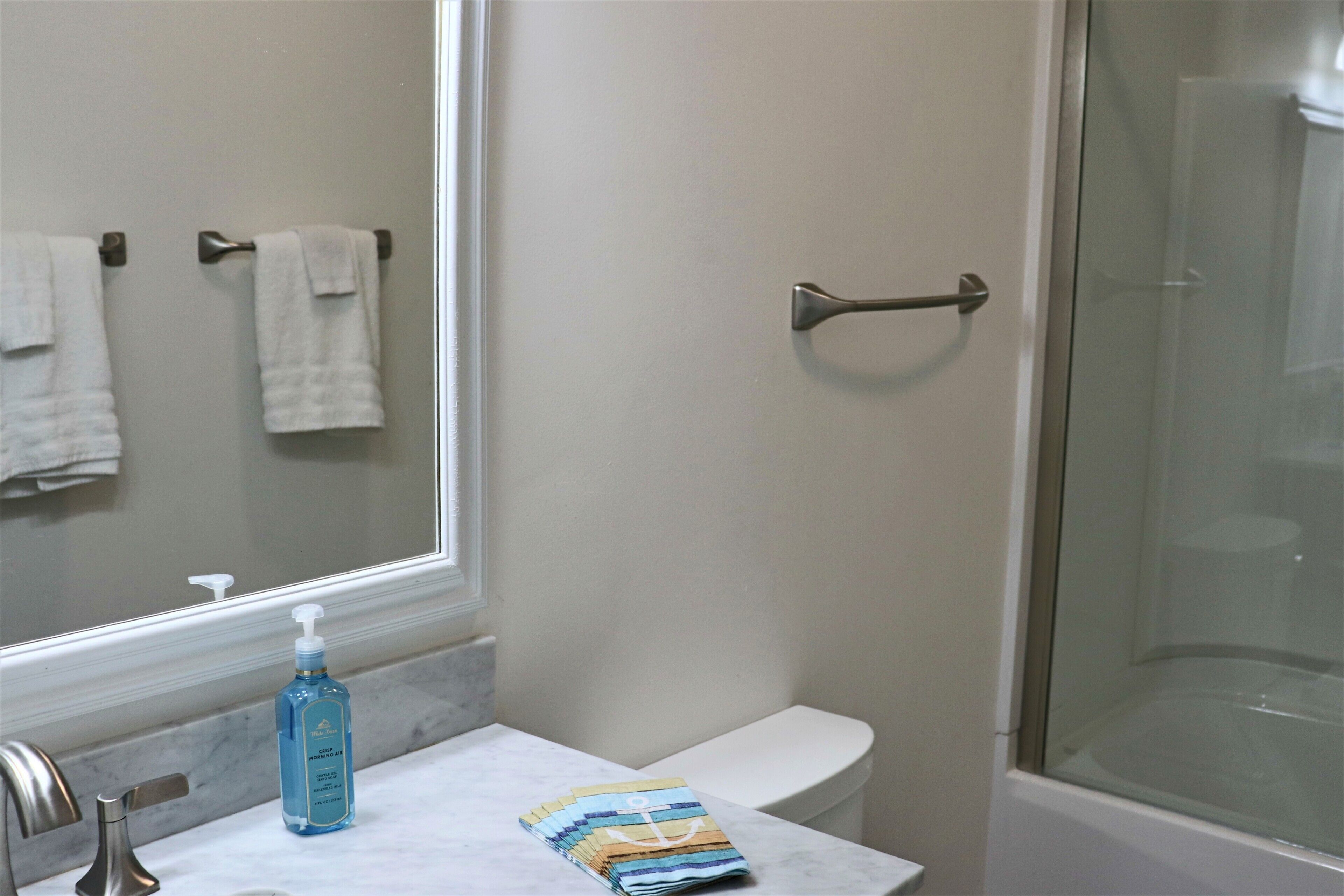 Ein Badezimmer mit Marmorplatte, Waschbecken, Toilette, Duschkabine aus Glas und einem Spiegel.
