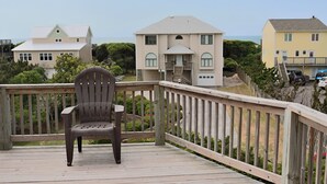Una terraza de madera con una sola silla, con vista a una zona residencial con casas y un cielo despejado.