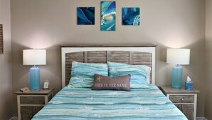 Un dormitorio con una cama, dos mesitas de noche, un cabecero y tres cuadros colgados en la pared.