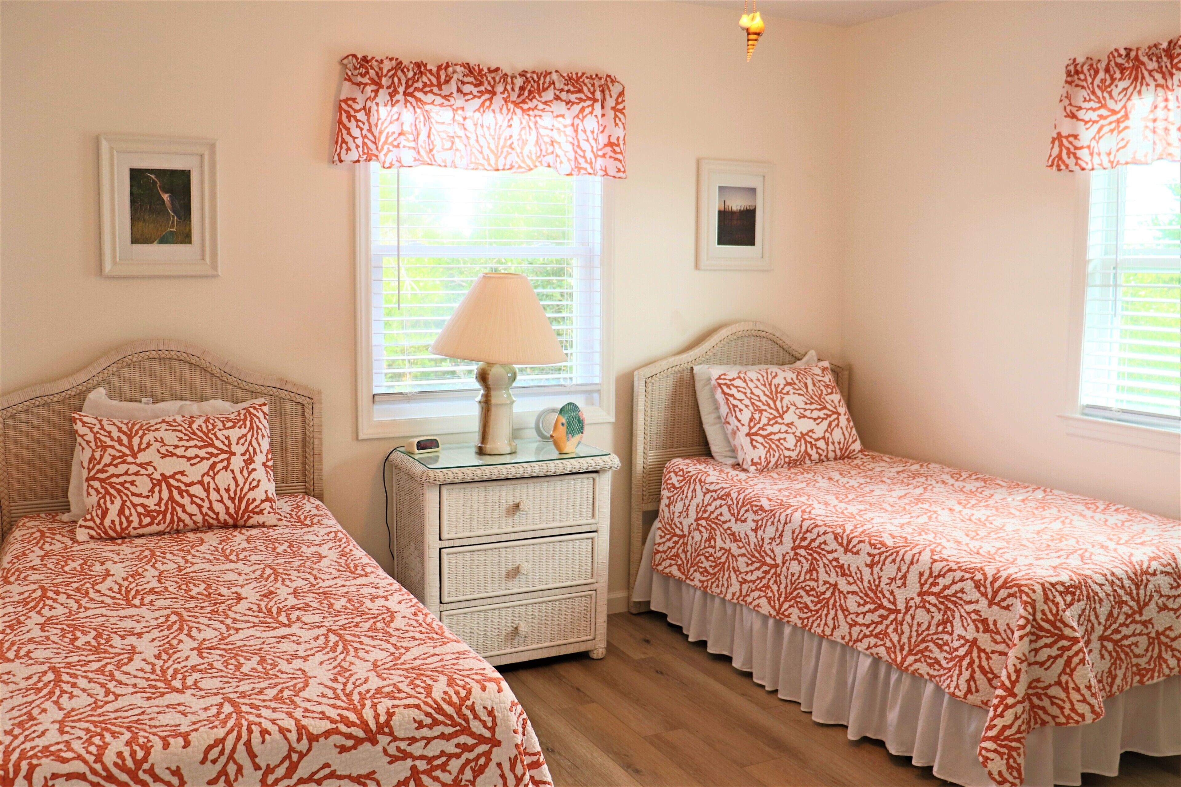 A bedroom with two beds, a nightstand, a lamp, and two framed pictures on the wall.