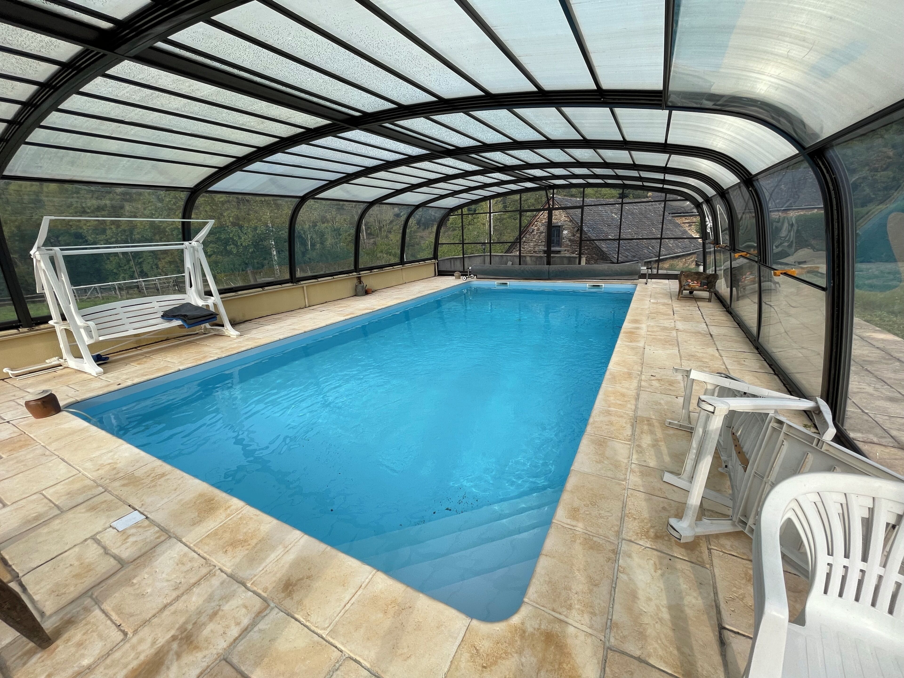 Une piscine couverte avec un toit en verre, un plongeoir et une vue sur le paysage environnant.