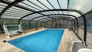 A covered swimming pool with a glass ceiling, a diving board, and a view of the surrounding landscape. - Cosy country side property with three cottages and covered swimming pool (Centres)