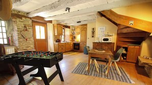 A cozy room with a foosball table, a dining table with chairs, and a kitchen area with wooden cabinets and a microwave. - Cosy country side property with three cottages and covered swimming pool (Centres)