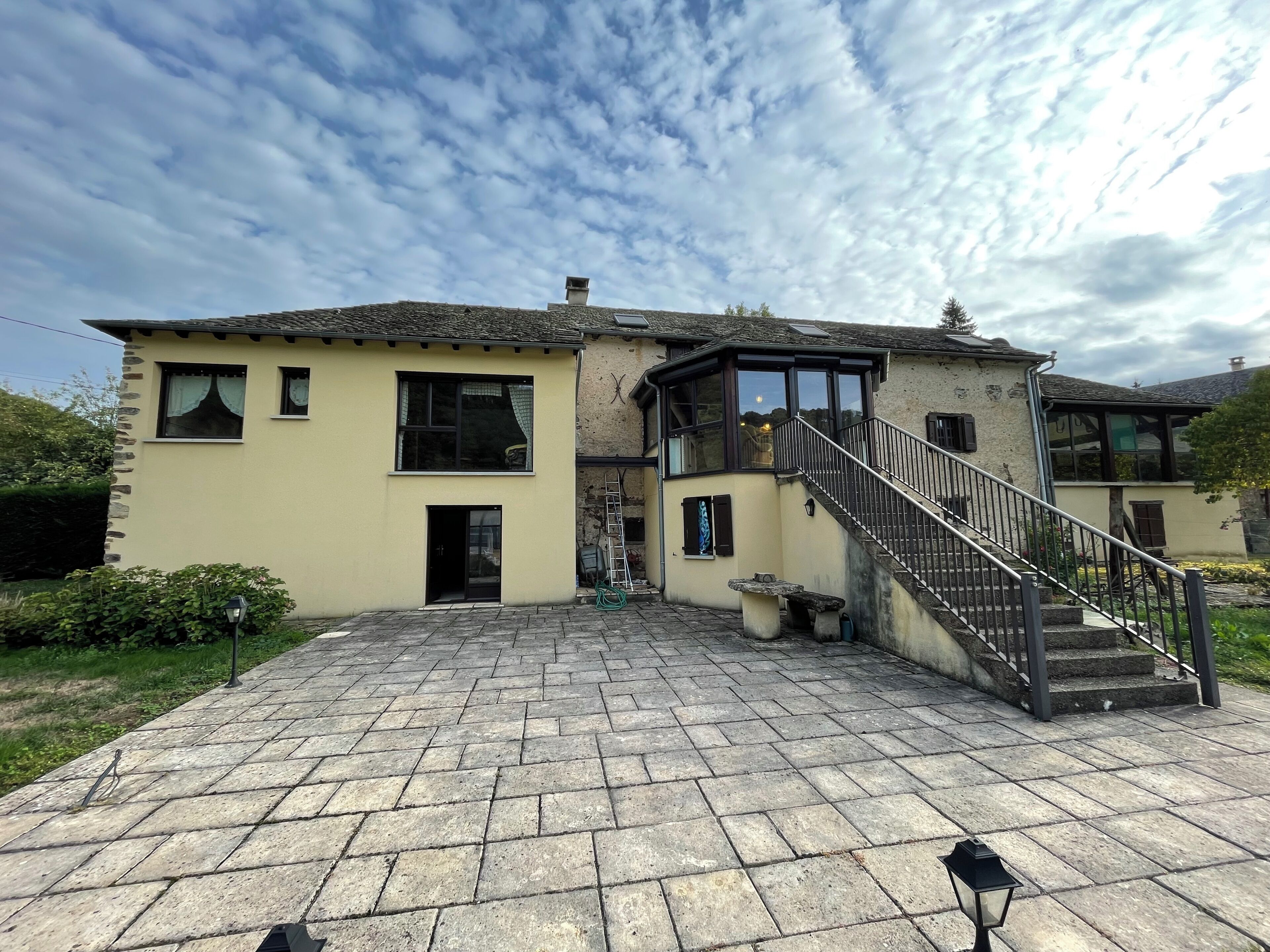 Une maison à deux étages avec une façade en pierre, un escalier central et une allée pavée.