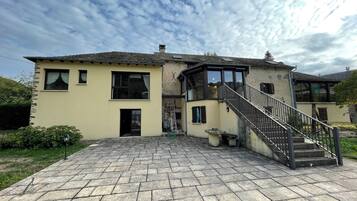 Une maison à deux étages avec une façade en pierre, un escalier central et une allée pavée.