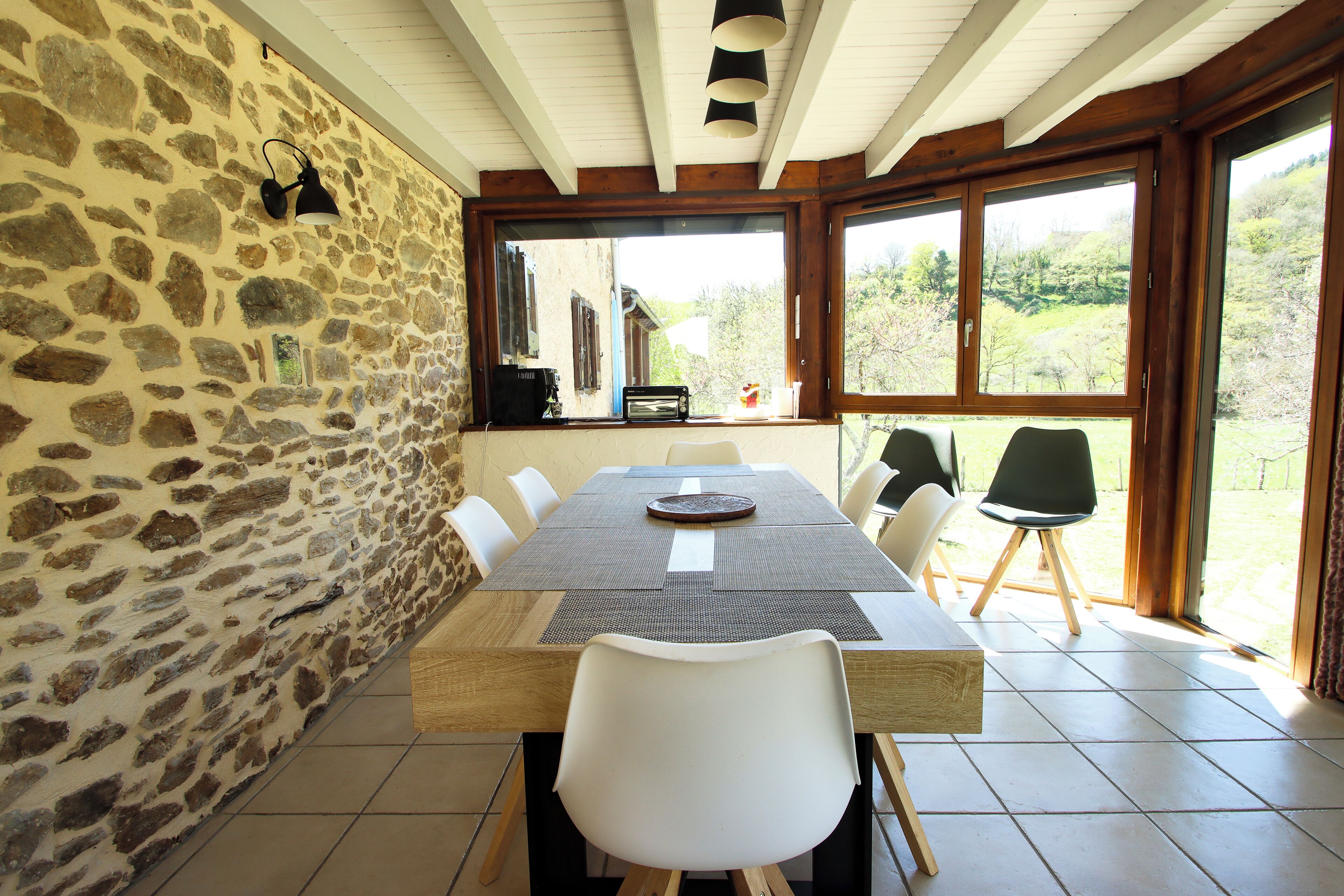 Un espace repas agrémenté d’un mur en pierre, d’un plafond en bois et de grandes fenêtres.