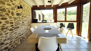 A dining area with a stone wall, wooden ceiling, and large windows. - Cosy country side property with three cottages and covered swimming pool (Centres)