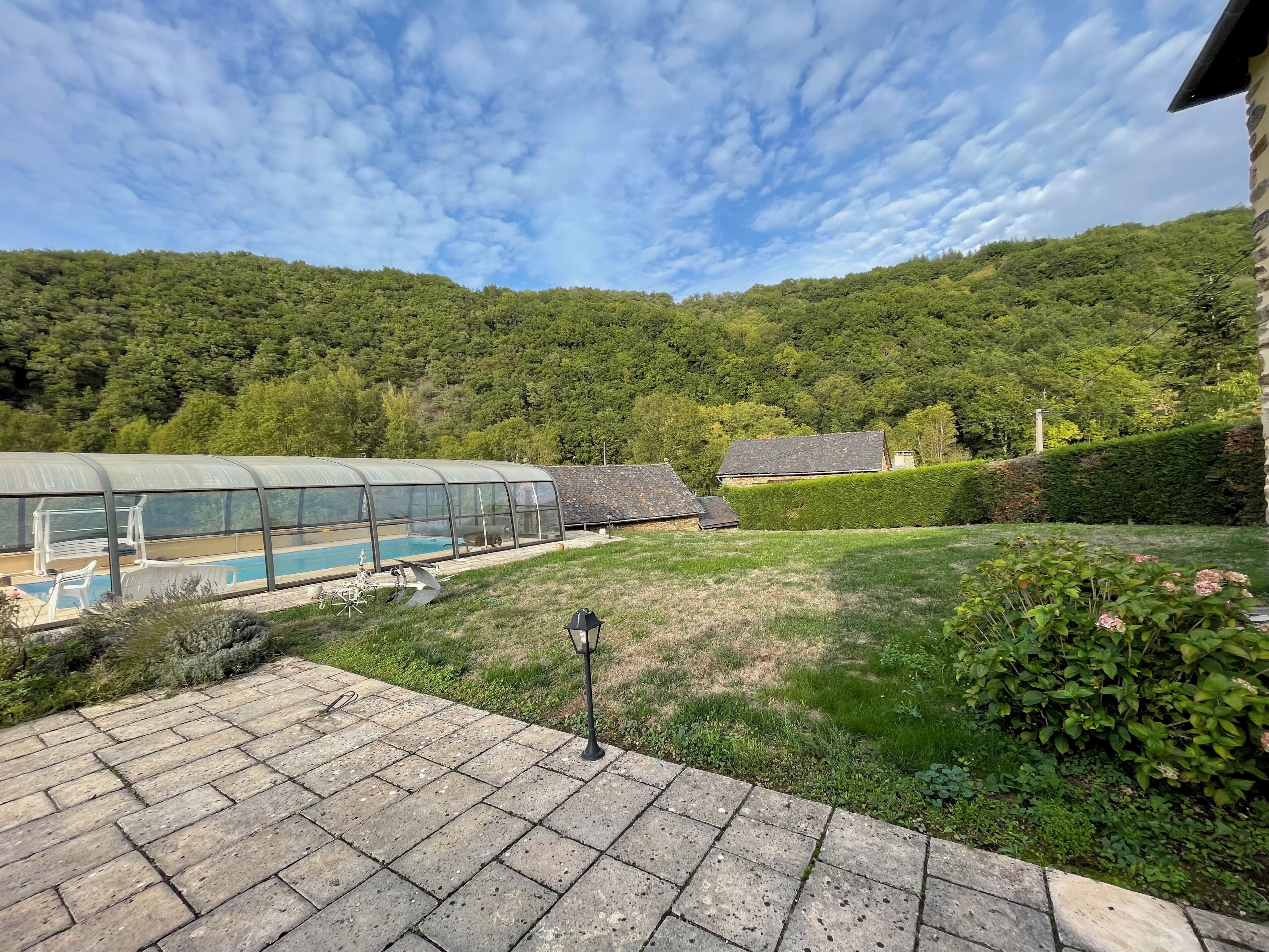 Un espace piscine protégé par une paroi de verre, un bâtiment en pierre et, en arrière-plan, une colline verdoyante.