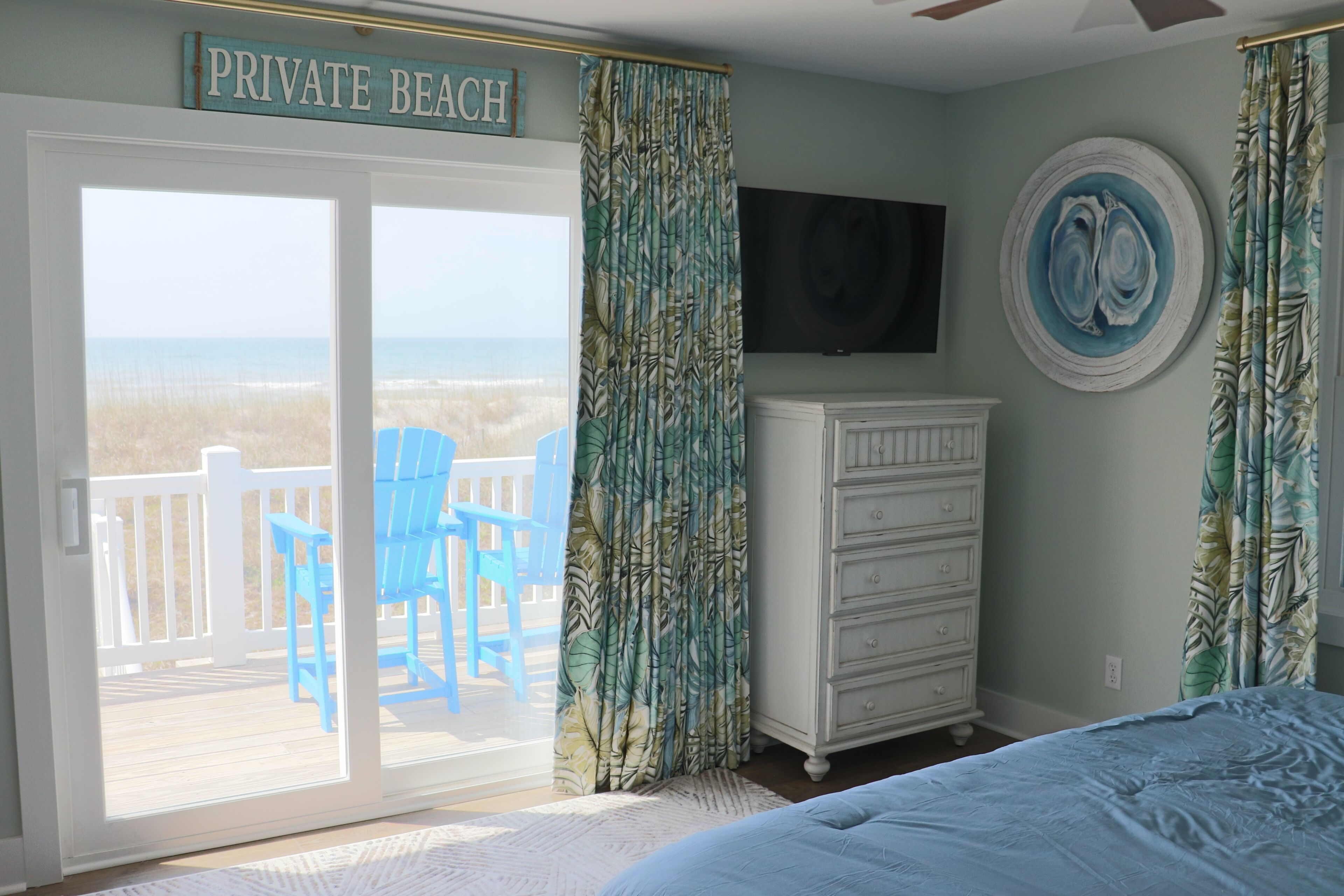 A bedroom with a sliding glass door to a deck, a dresser, a television, and a decorative plate on the wall.