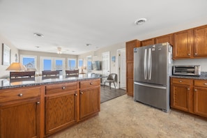 A kitchen with wooden cabinets, a stainless steel refrigerator, a built-in oven, and a dining area with a table and chairs. - Spacious Oceanview Home | Short Walk to Beach | Pool (Emerald Isle)