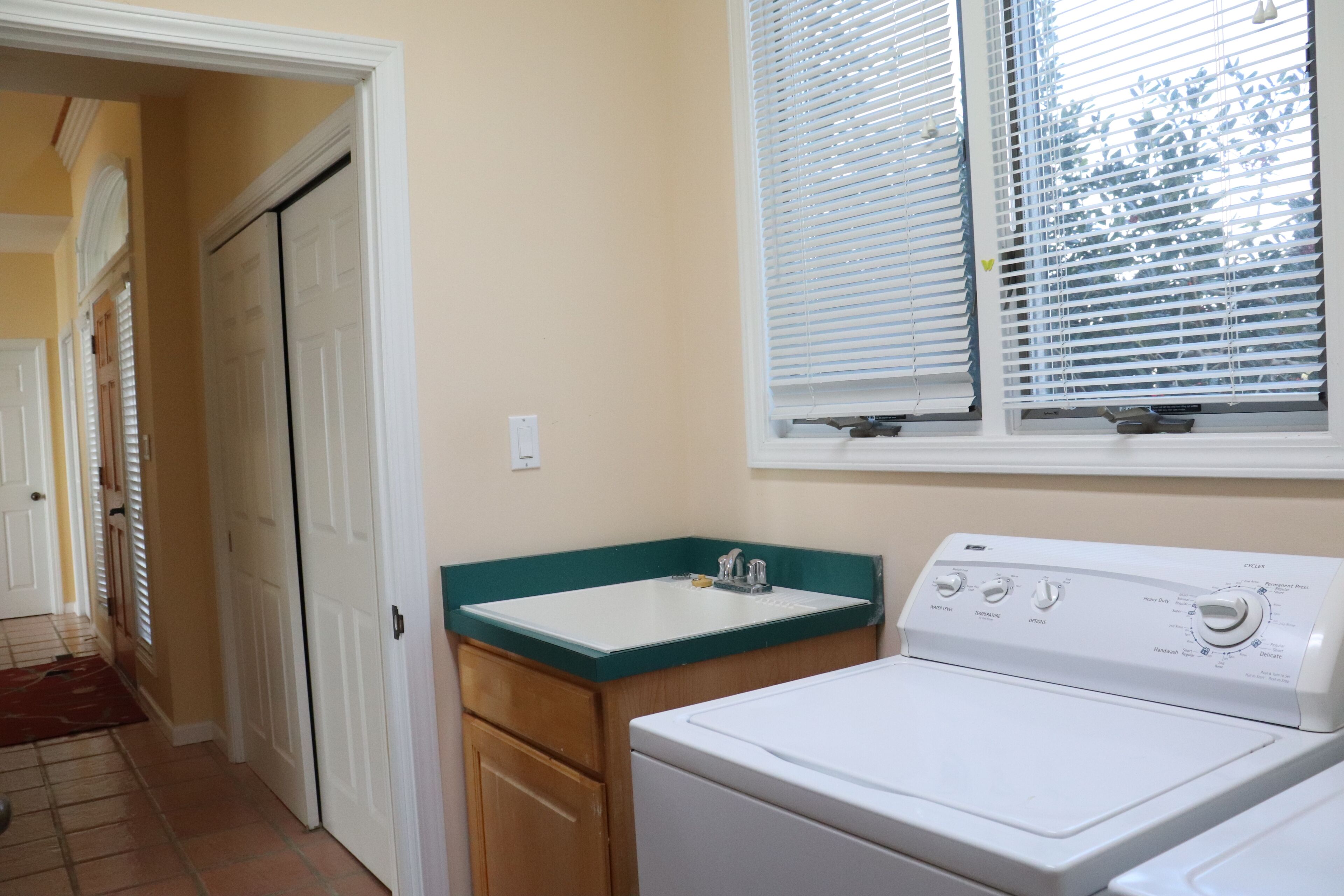 A laundry area with a washing machine, a sink, and a window with blinds.