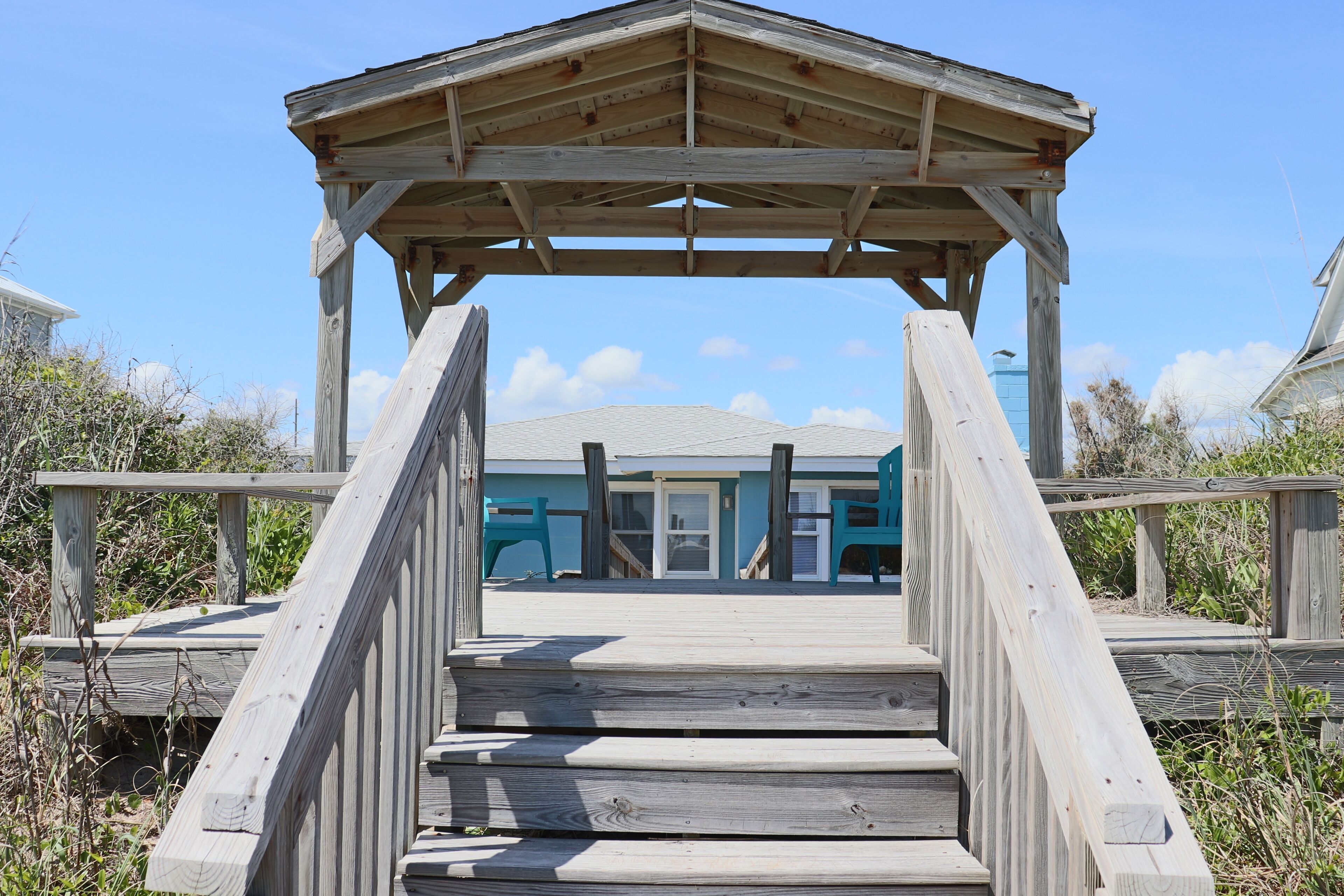 A wooden boardwalk leading to a beach house with a covered area.