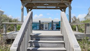 Un muelle de madera que lleva a una casa de playa con un porche cubierto.