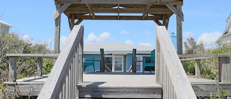 A wooden boardwalk leading to a beach house with a covered area.