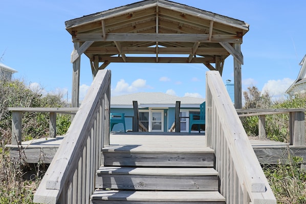 Ein hölzerner Steg führt zu einem Strandhaus mit überdachter Veranda.