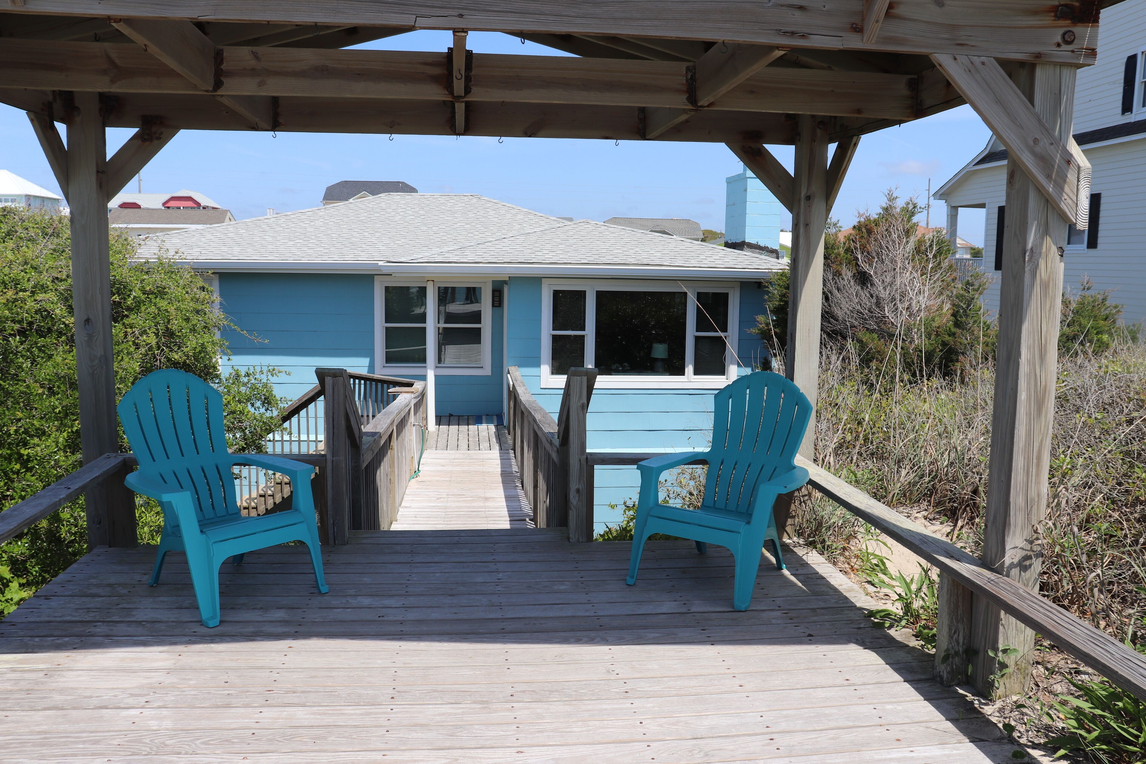 A wooden deck with two chairs and a table, leading to a house with a blue exterior.