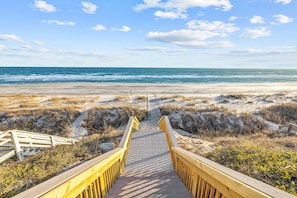 A wooden boardwalk leading to a beach with sand dunes and the ocean in the background.