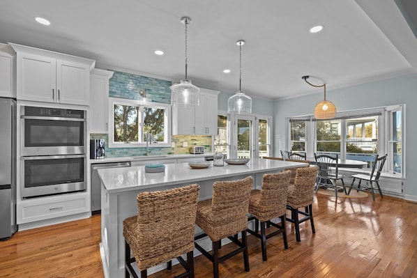 A modern kitchen with stainless steel appliances, a large island with bar stools, and large windows offering views of the outdoors.