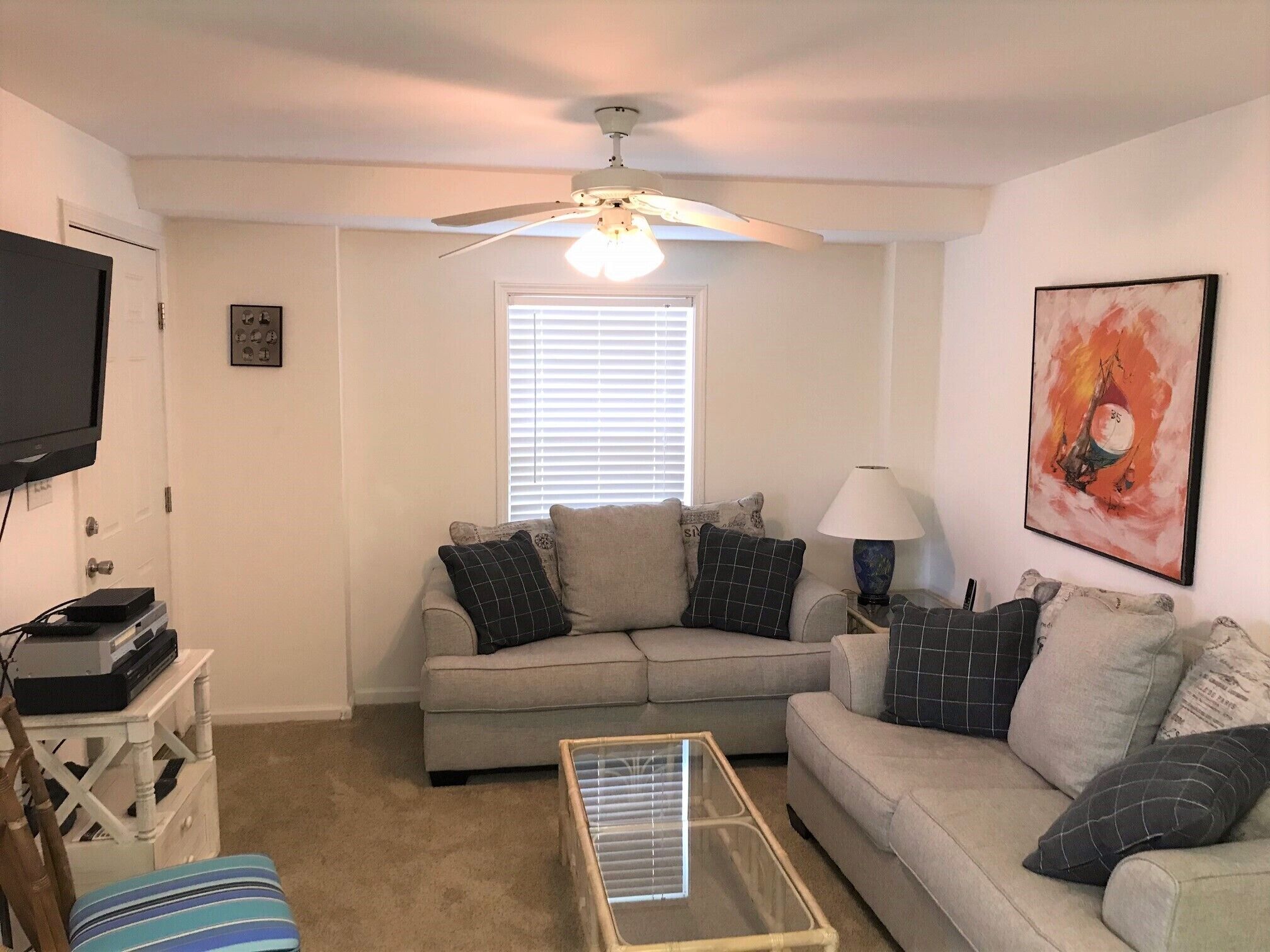 A living room with a ceiling fan, a television, a window with blinds, a sofa, a coffee table, and a lamp.