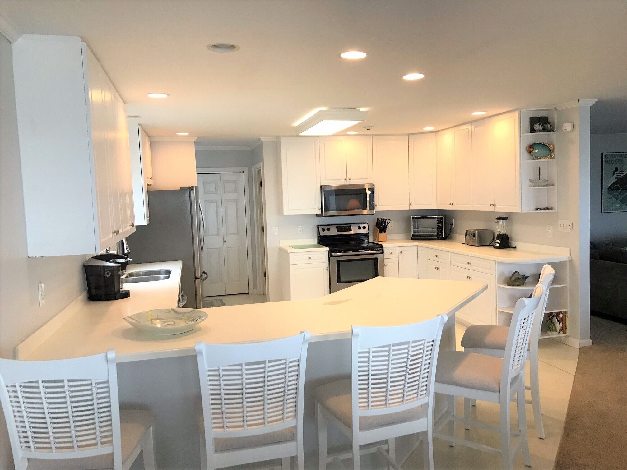 Une cuisine moderne avec des meubles blancs, un îlot central doté de chaises et des appareils électroménagers intégrés.