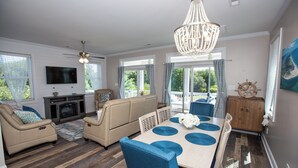 A spacious living room with a fireplace, a dining area with blue chairs, and a chandelier. - Island Retreat, The Ultimate Emerald Isle Getaway! (Emerald Isle)