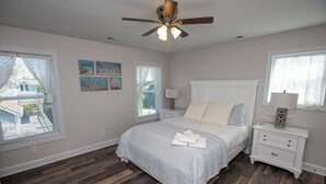 A bedroom with a bed, nightstands, a ceiling fan, and artwork on the walls. - Island Retreat, The Ultimate Emerald Isle Getaway! (Emerald Isle)