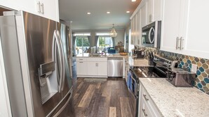 A modern kitchen with stainless steel appliances, white cabinetry, and a stone backsplash. - Island Retreat, The Ultimate Emerald Isle Getaway! (Emerald Isle)