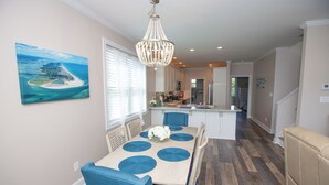 A modern kitchen with a central island, a dining area with blue placemats, and a chandelier. - Island Retreat, The Ultimate Emerald Isle Getaway! (Emerald Isle)