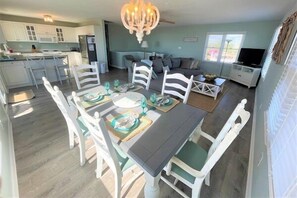 Ein Essbereich mit Tisch für vier Personen, eine Küche im Hintergrund und eine Wohnbereich mit Sofa und Fernseher.