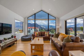 Ein großzügiges Wohnzimmer mit einem großen Fenster, einem Sofa, einem Couchtisch und einem Fernseher.