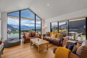 Ein geräumiges Wohnzimmer mit großen Fenstern, einem Ledersofa, einem Holztisch und Blick auf Berge.
