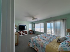 A bedroom with a bed, a television, a ceiling fan, and a view of the beach. - Ocean Front Beach Home 4BR – Views, Decks & Beach Access (Emerald Isle)
